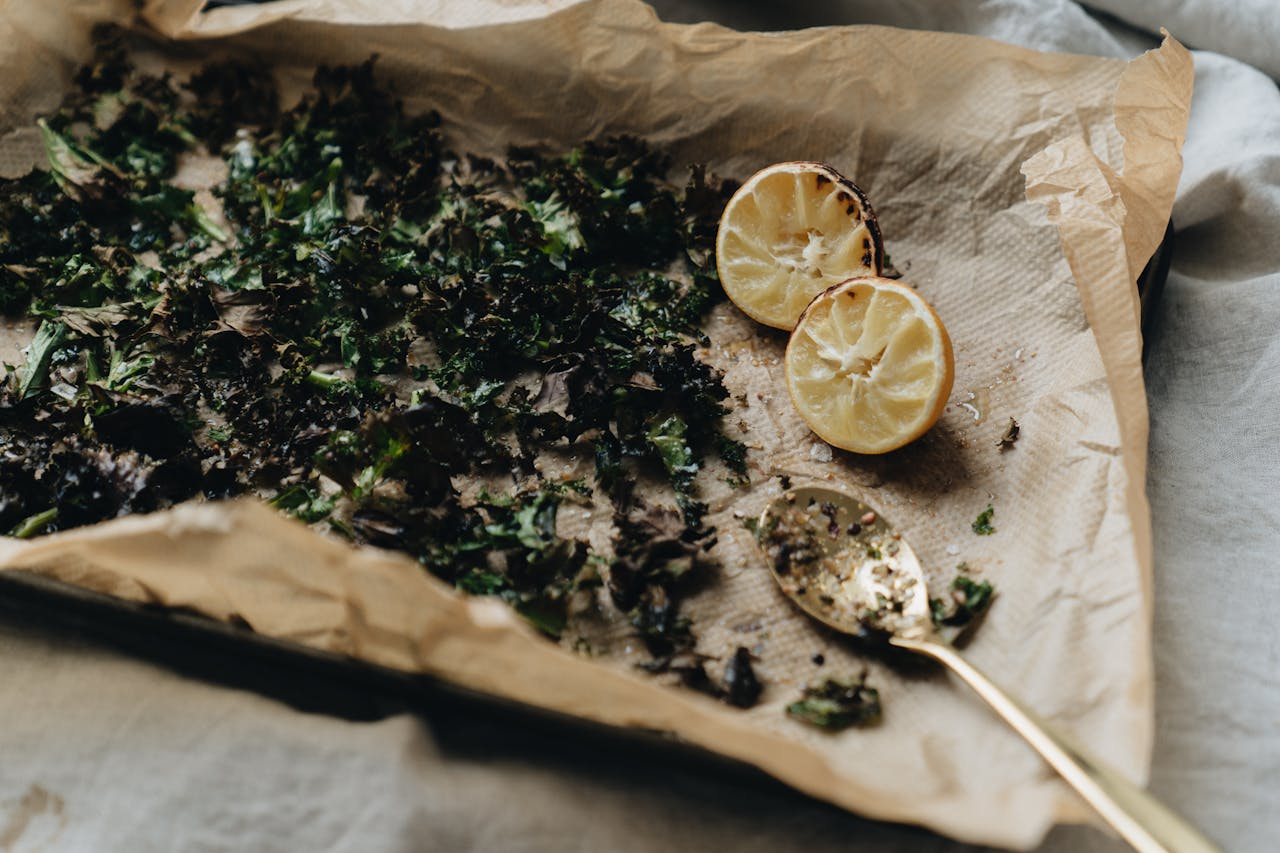 A minimalistic image of roasted herbs and lemon halves on a lined baking sheet with a spoon.
